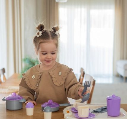 Smiling young girl plays with colorful toy tableware at home, enjoying a playful afternoon.