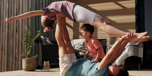 Father and kids doing yoga outdoors on a patio, balancing poses together.